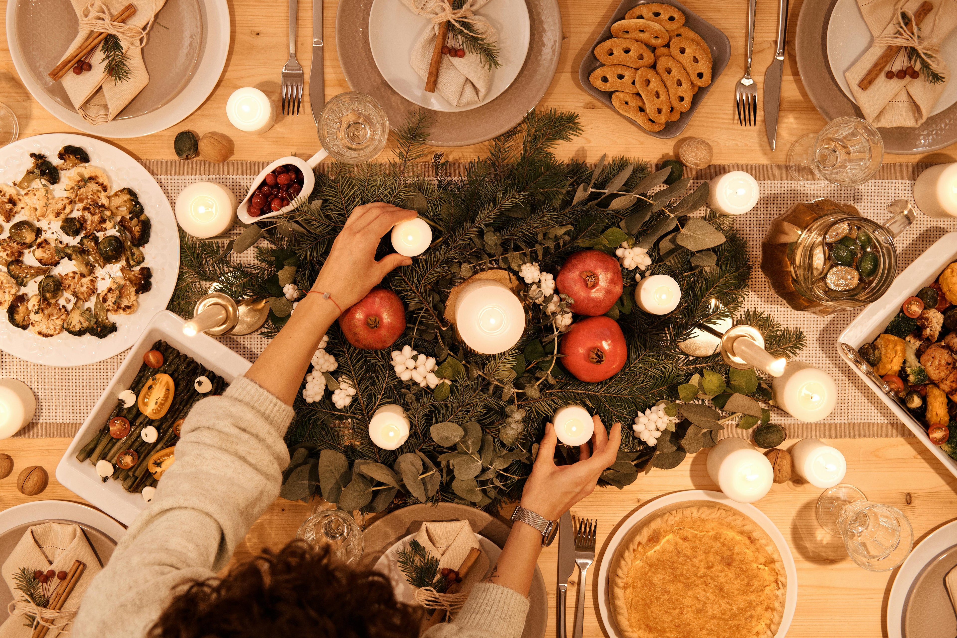 christmas dinner table with candles, greenery, pomegranates, roasted vegetables, holiday dishes, and festive place settings